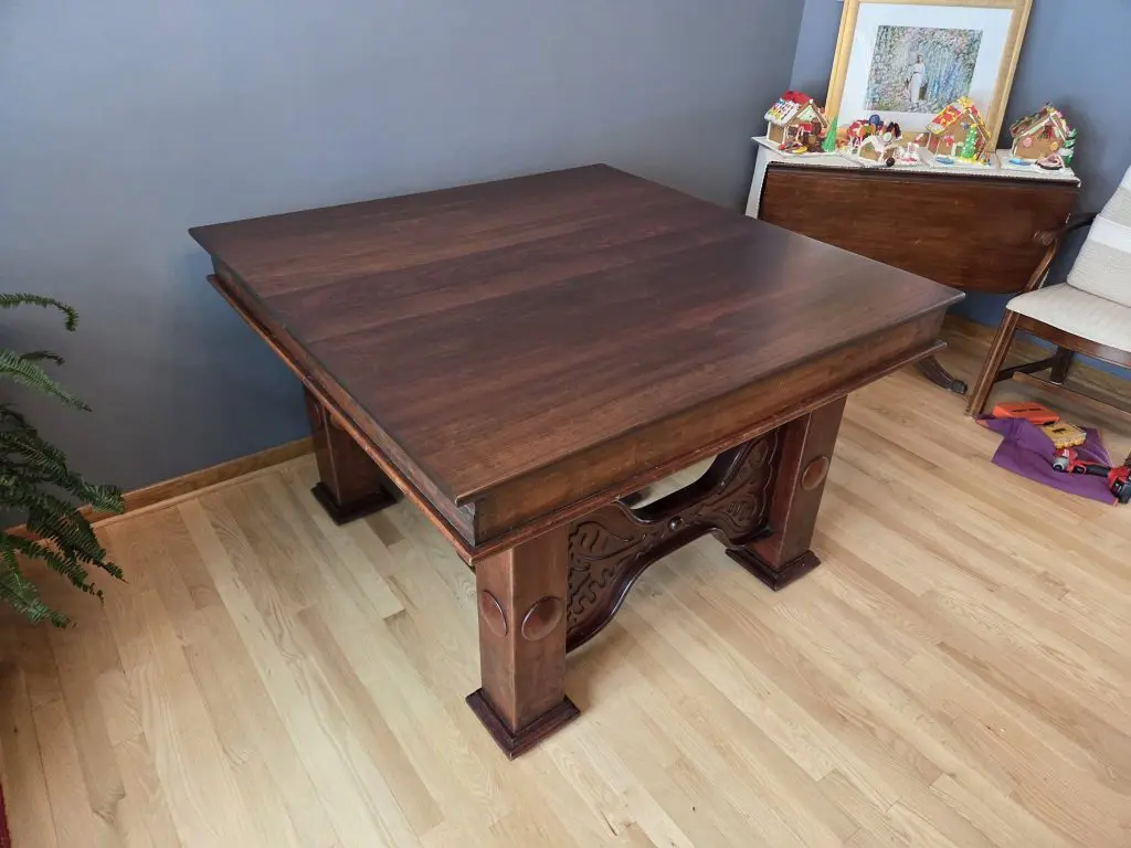 600347246_1414122677373712_570637057915604480_n - Four Fields Furniture Dark wooden dining table with ornate carved legs in a blue-walled room; a sideboard holds gingerbread houses and a framed picture on top, with a chair nearby.