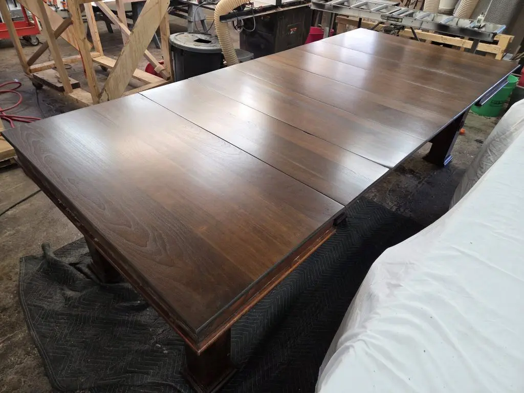 600549766_1414122720707041_318249122399983498_n - Four Fields Furniture Long dark-stained wooden tabletop panels laid out in a woodworking shop for finishing, with tools and equipment in the background.