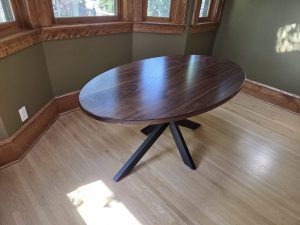 Oval walnut dining table with black steel base in a bay window, Minneapolis–St. Paul